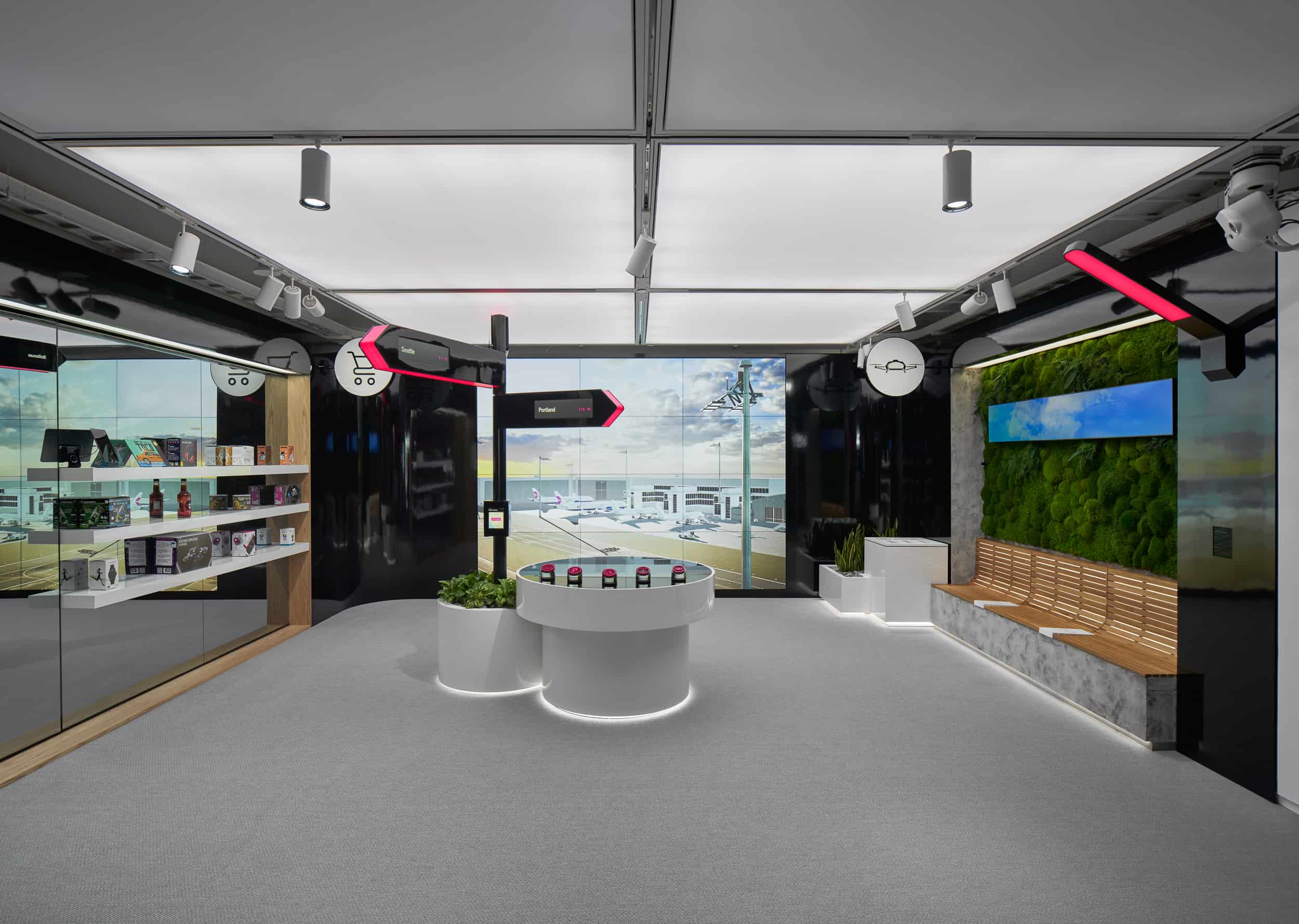 Sleek black & white showroom with shelves, central round table of colorful items, wall greenery, and bright LED lighting for a modern vibe.